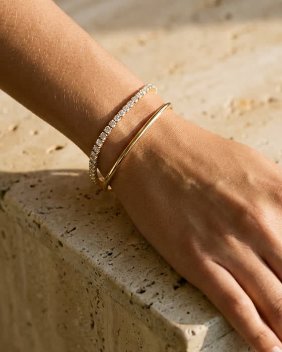 A diamond line bracelet worn beside a polished gold bangle on a travertine ledge
